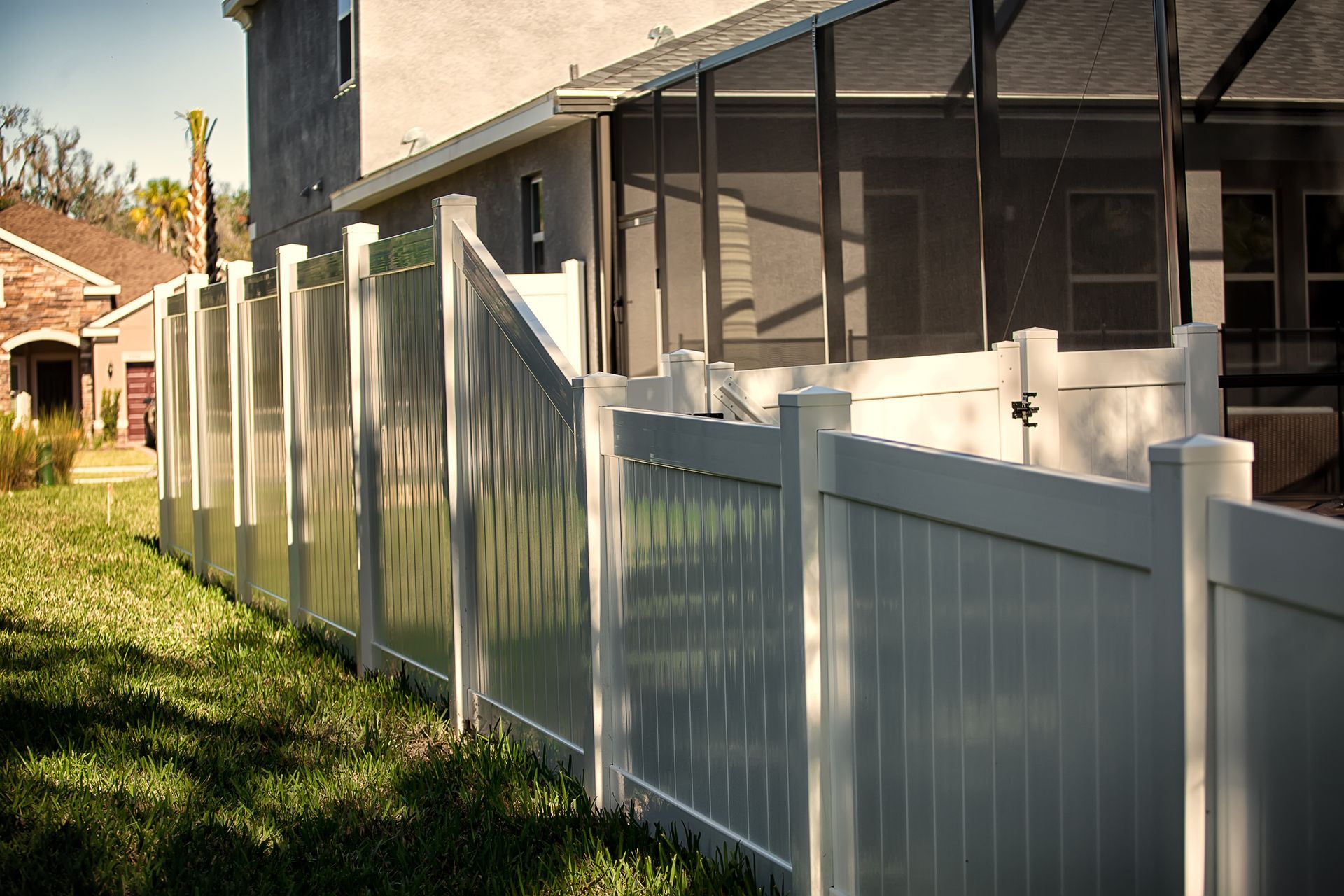 White vinyl fence bordering a grassy yard next to a house with a screened-in porch.