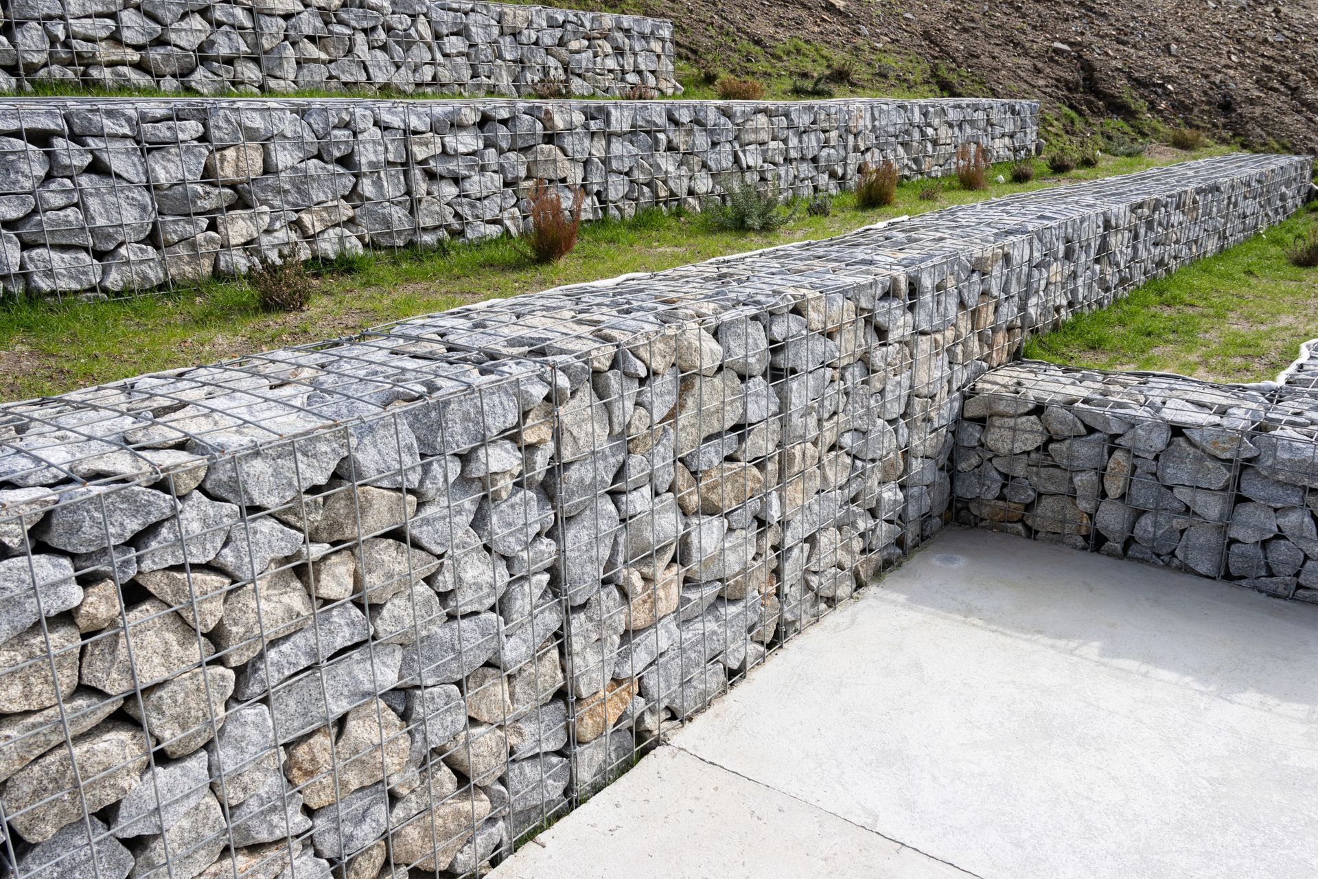 Gabion walls with stone fill, terracing a hillside. Gray rocks and wire mesh.