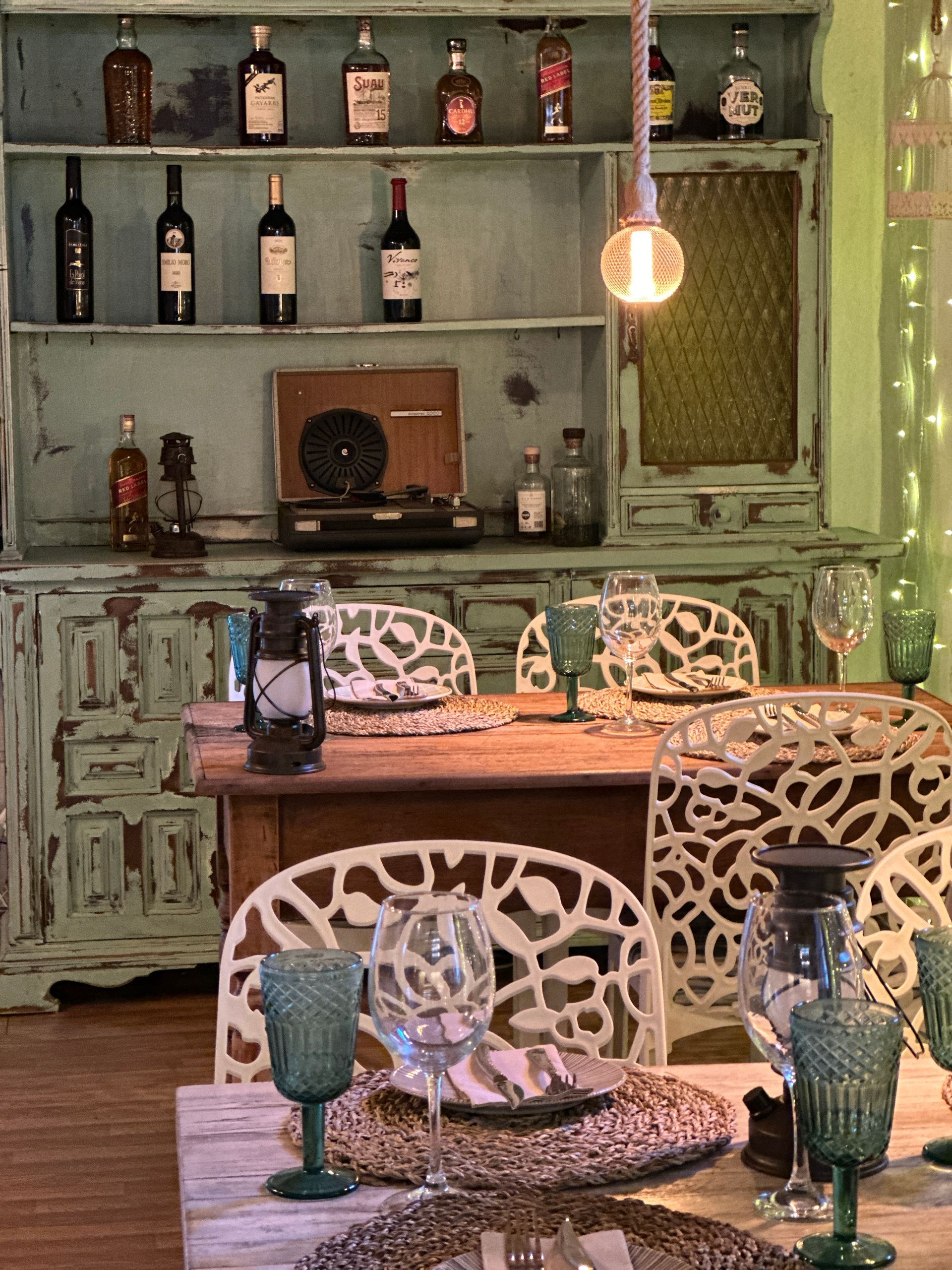 Un comedor con mesa, sillas, vasos y un tocadiscos.