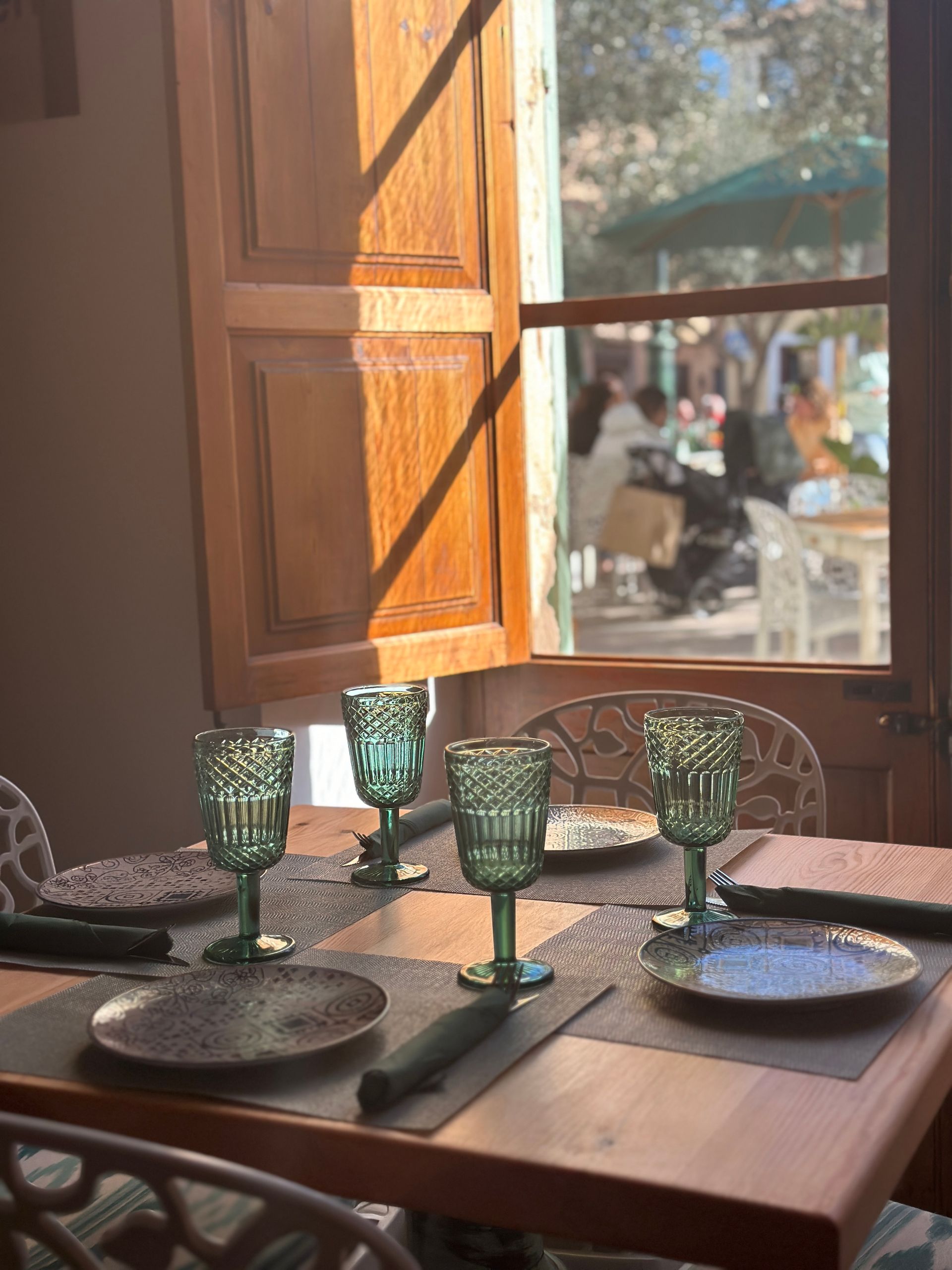 Una mesa puesta con platos y copas de vino frente a una ventana.