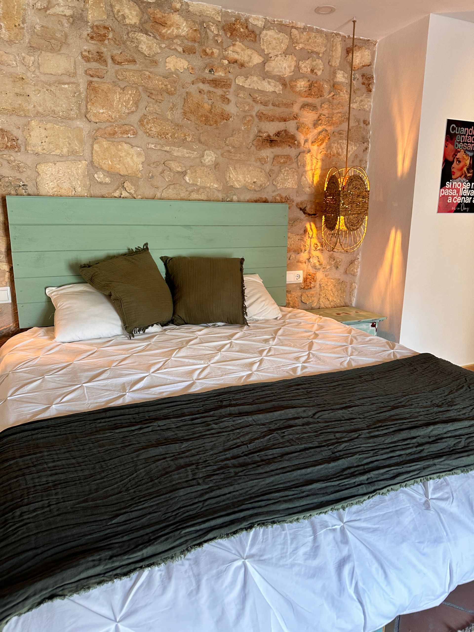 Una cama con cabecero verde y almohadas en un dormitorio con una pared de piedra.