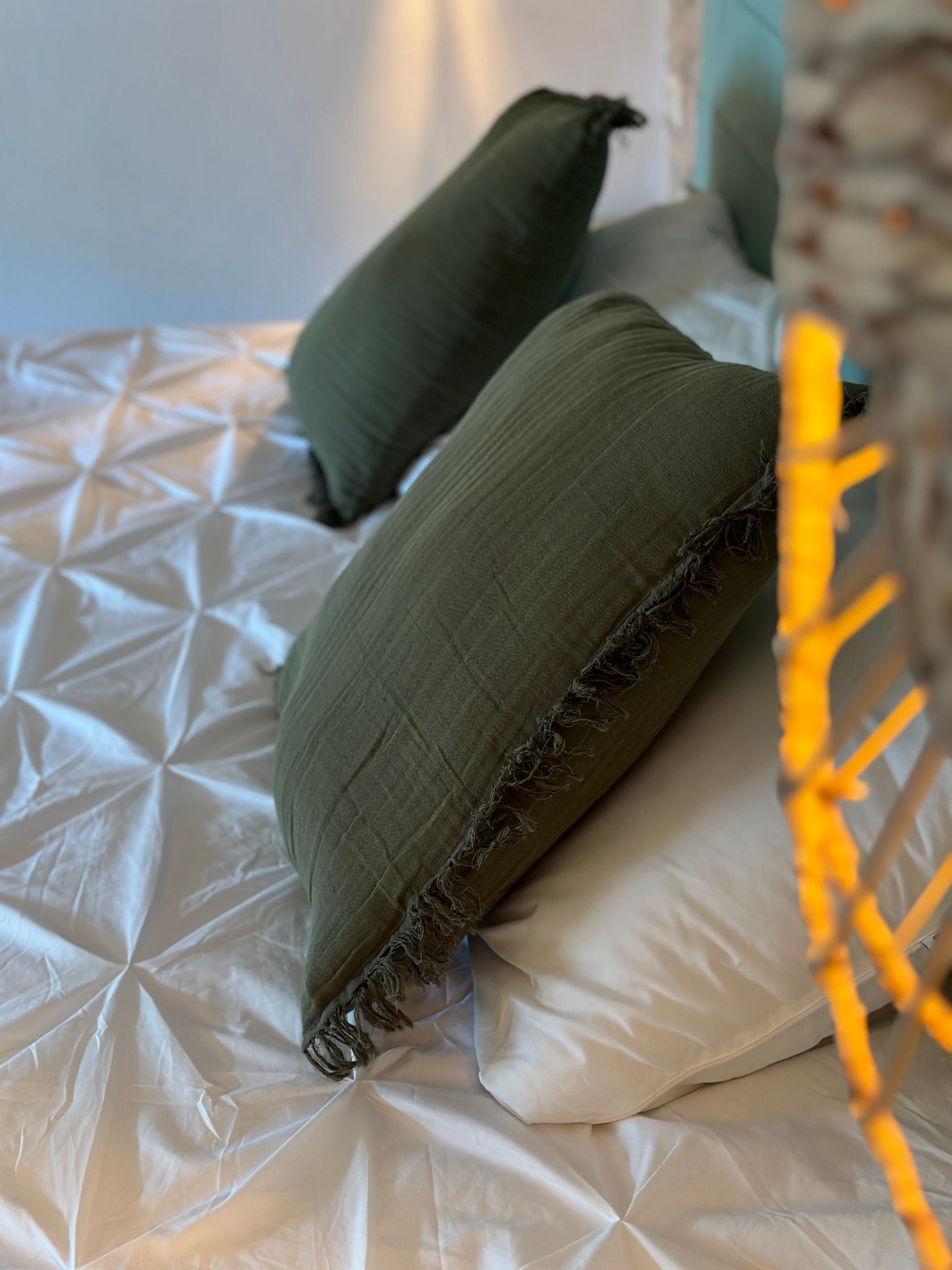 Una cama con sábanas blancas y almohadas verdes.