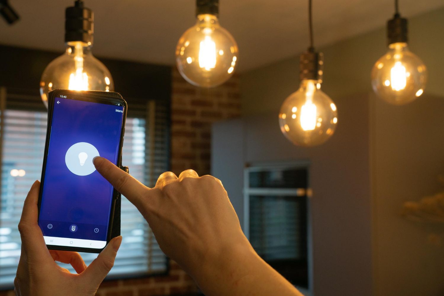Person using a smartphone to control Edison-style light bulbs in a room, shown lit.