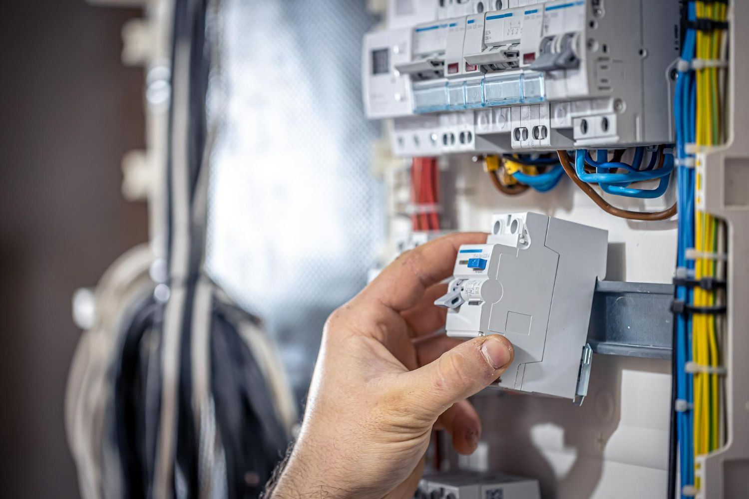 A person is holding a circuit breaker in their hand in front of an electrical box.