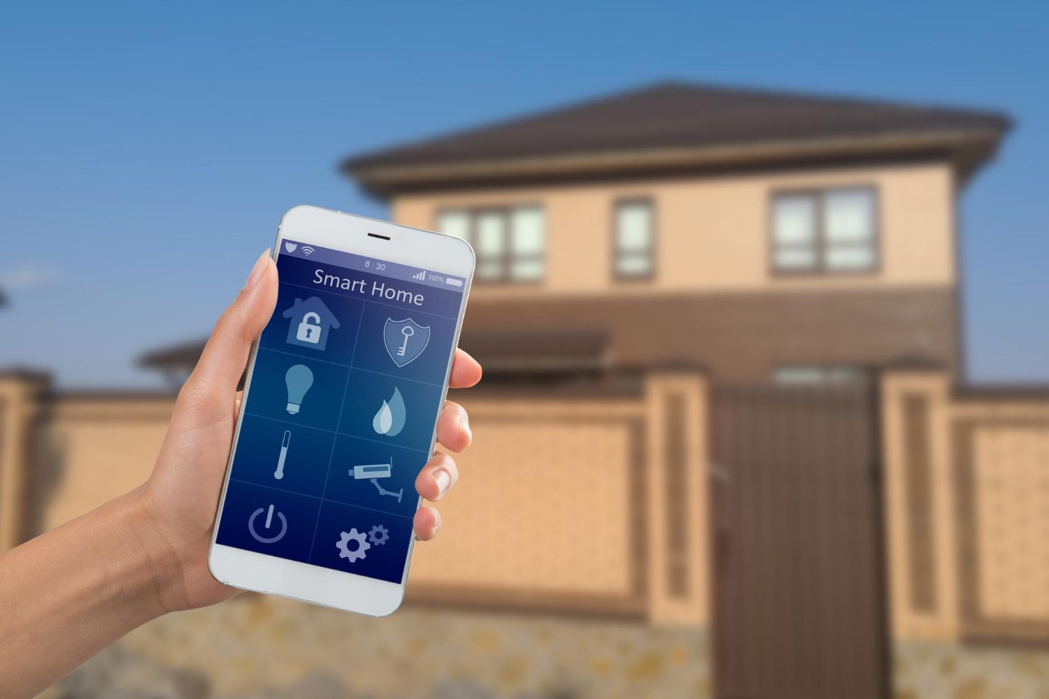 A hand holds a smartphone displaying a smart home control app in front of a modern house.