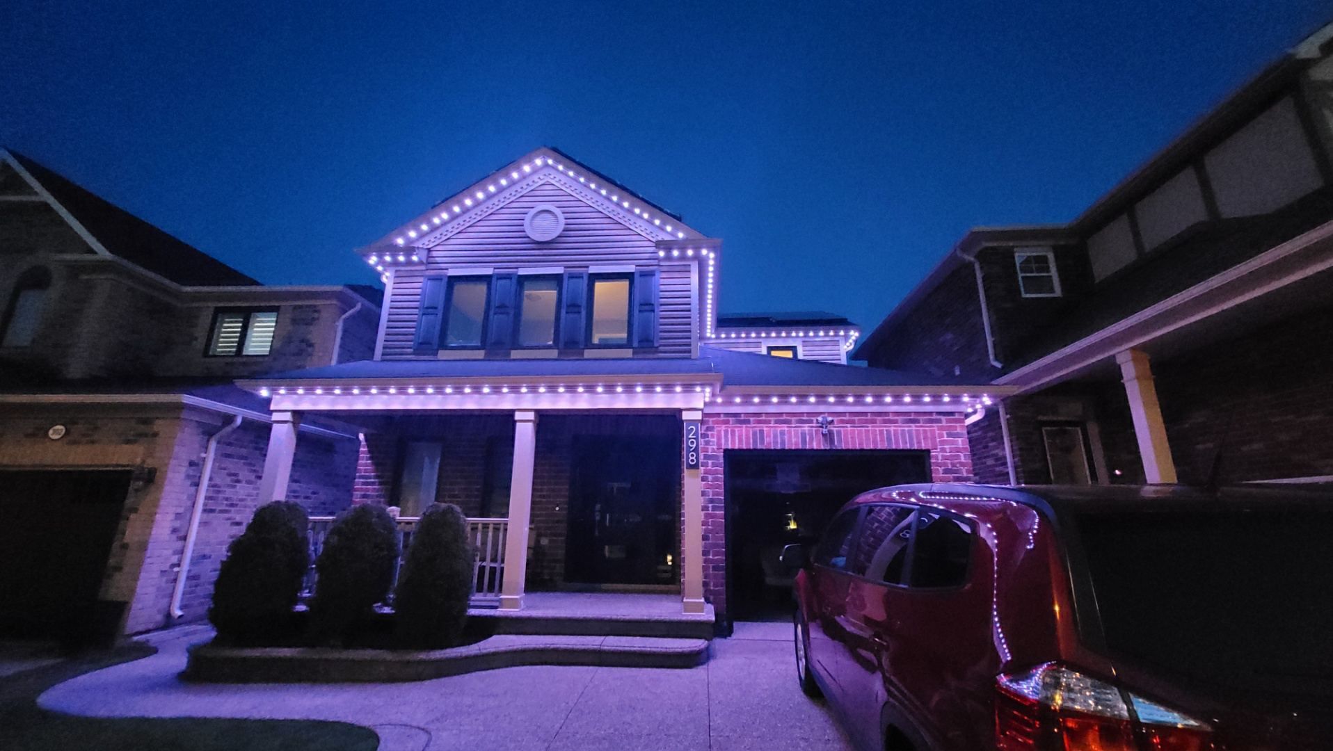 A suburban house at dusk, decorated with glowing purple LED lights along the roofline and porch.