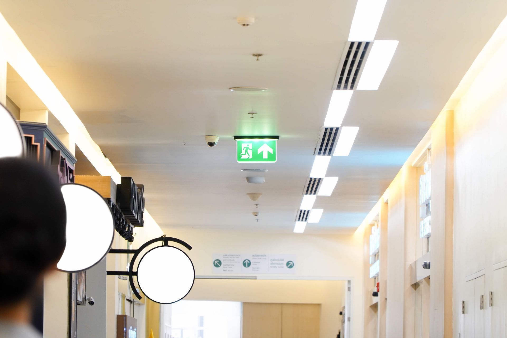 A person is walking down a hallway with a green exit sign on the ceiling.