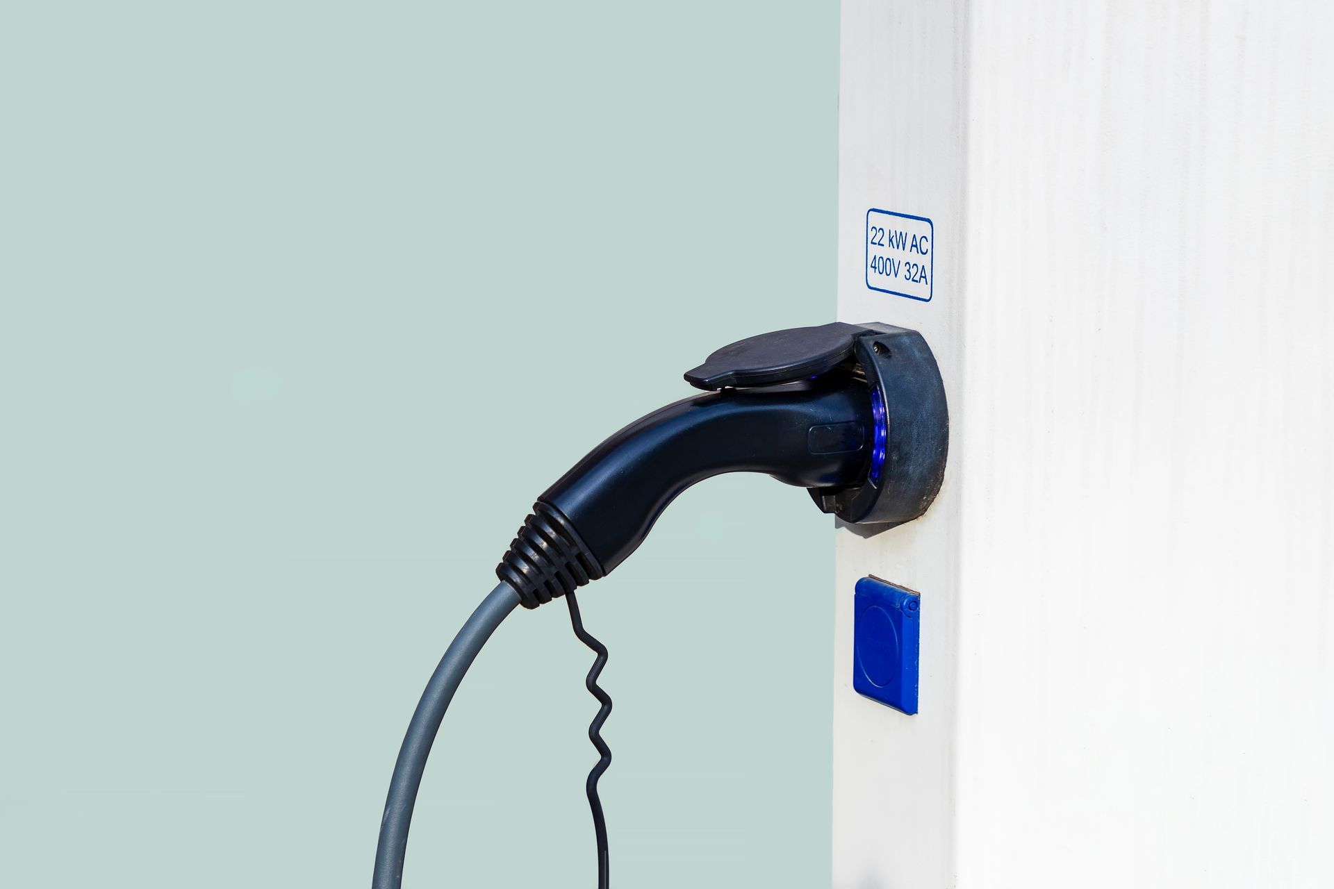 Electric vehicle charger on a white column, with a blue light and a blue button.