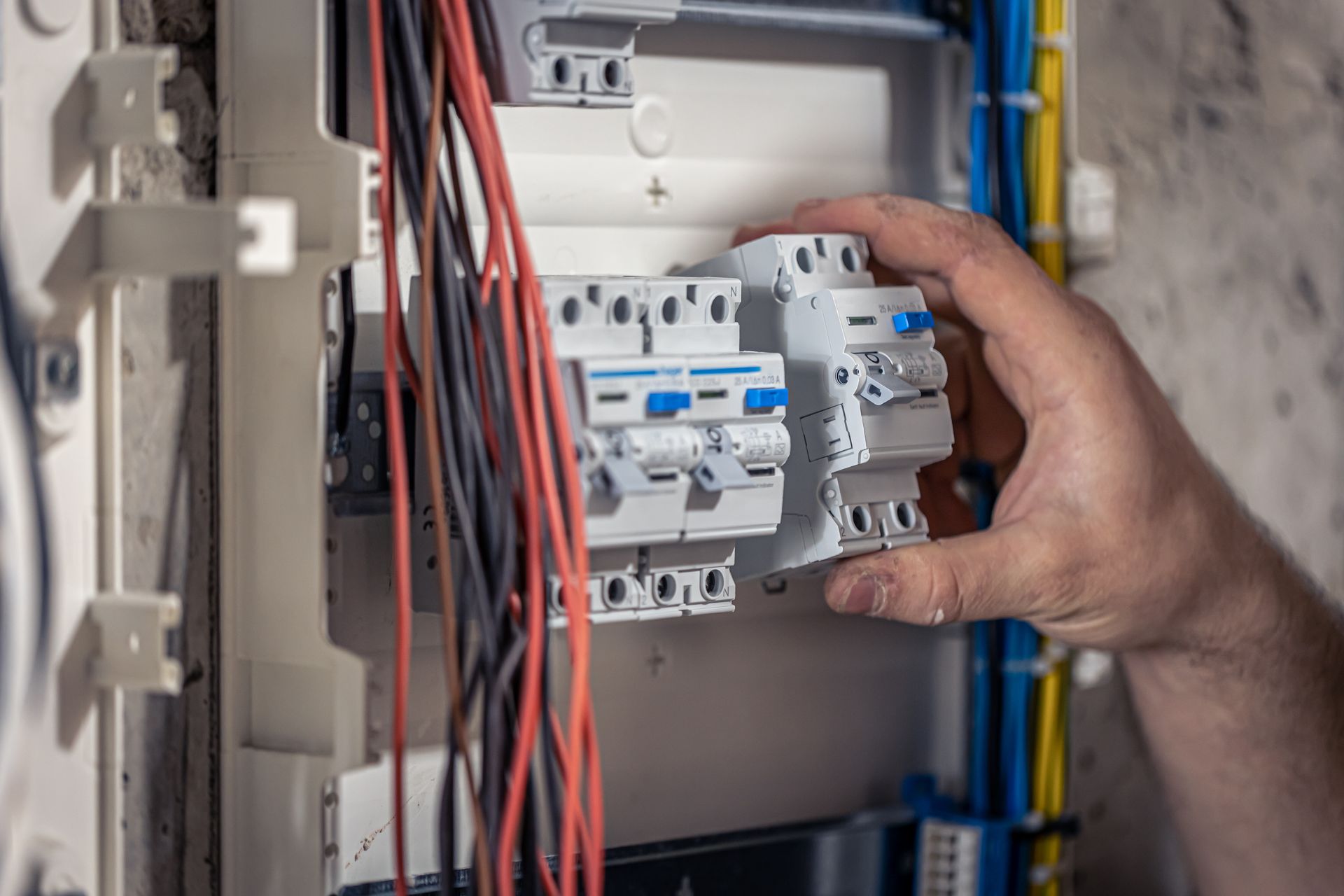 A person's hand installing a circuit breaker in an electrical panel. Red, black, and blue wires are visible.