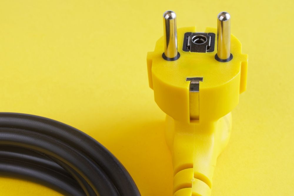 Yellow electrical plug with black cord, against a yellow background.