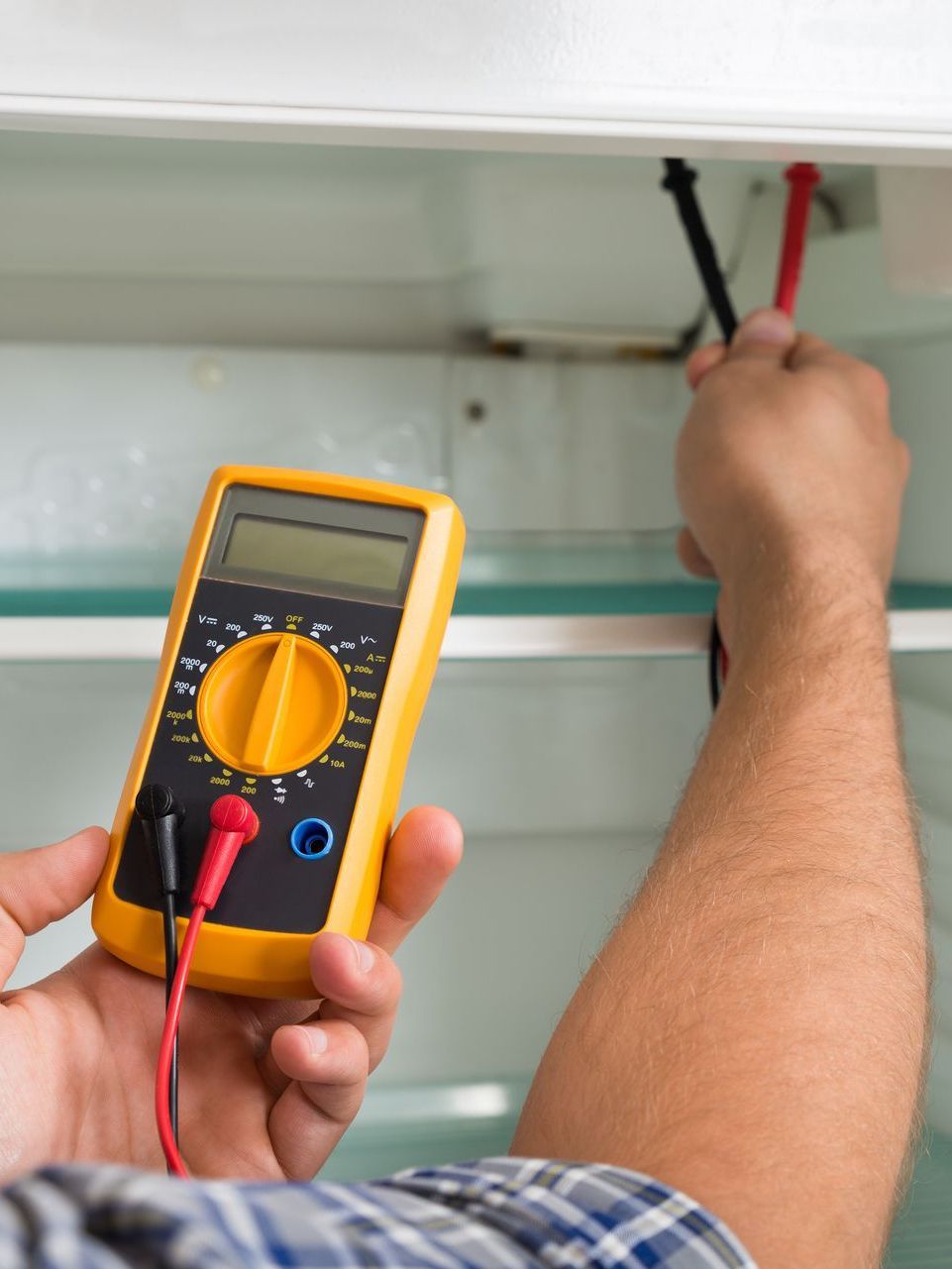 A man is using a digital multimeter to test a fridge
