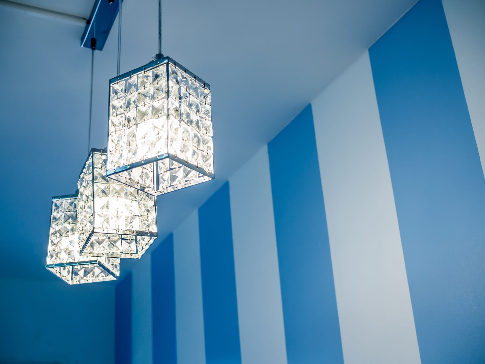 Three crystal pendant lights hang from a ceiling in front of blue and white striped wall.