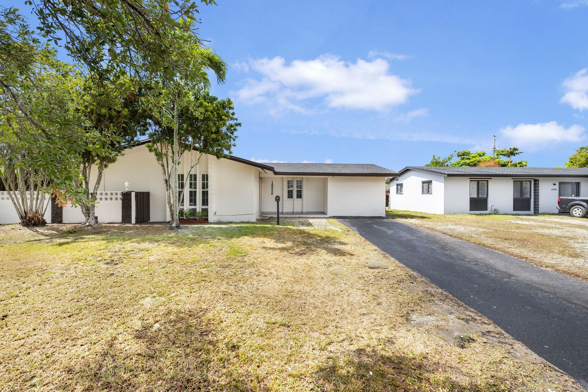 White house with a dark driveway and brown lawn on a sunny day.