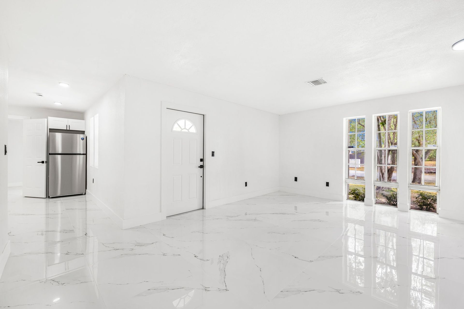 Bright white interior with tile floor, stainless steel fridge, door, and windows overlooking greenery.
