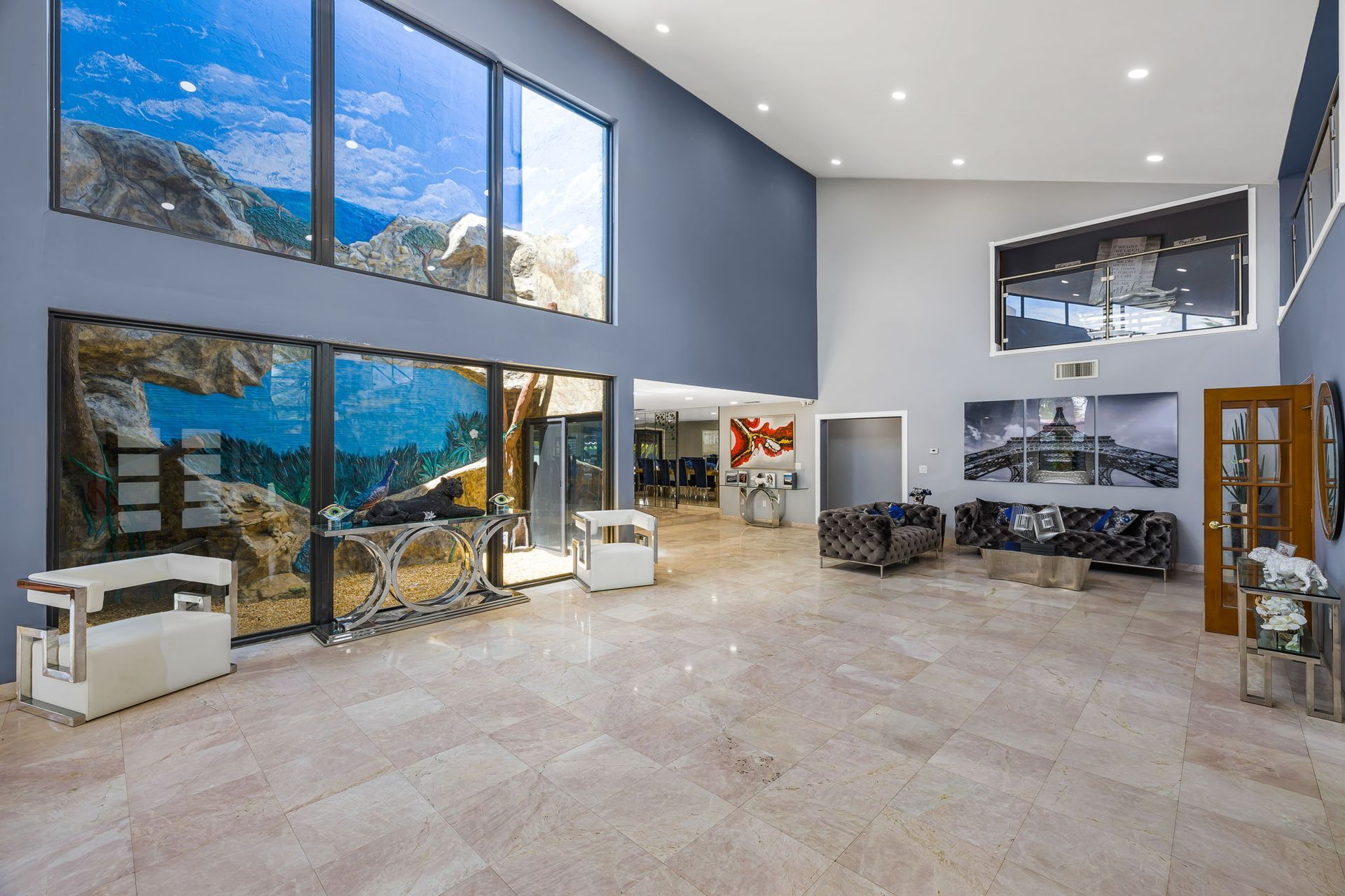 Spacious modern interior with large windows, high ceilings, marble floors, artwork, and furniture.