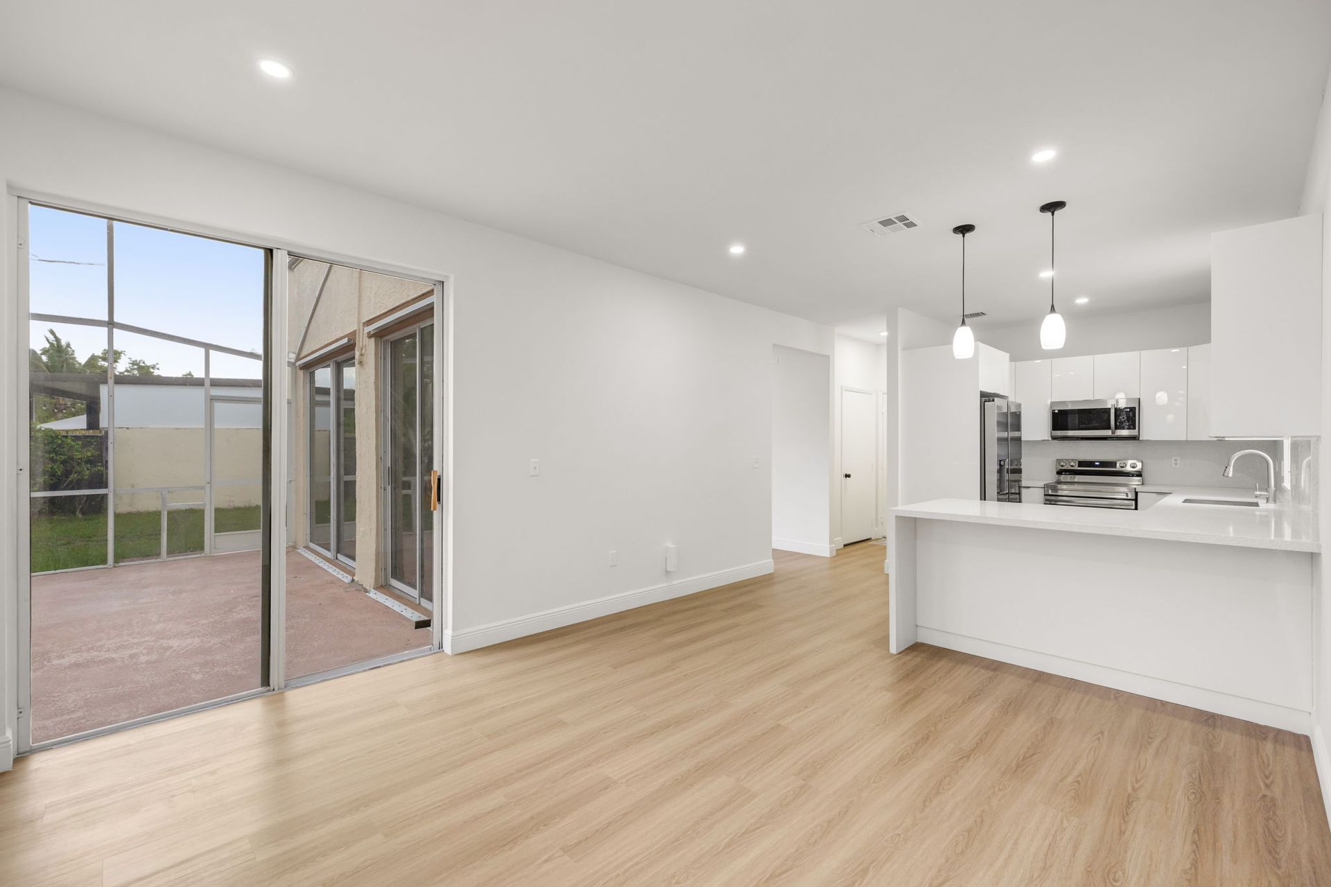 A modern, minimalist kitchen featuring glossy white cabinets, stainless steel appliances, and a glass block window.