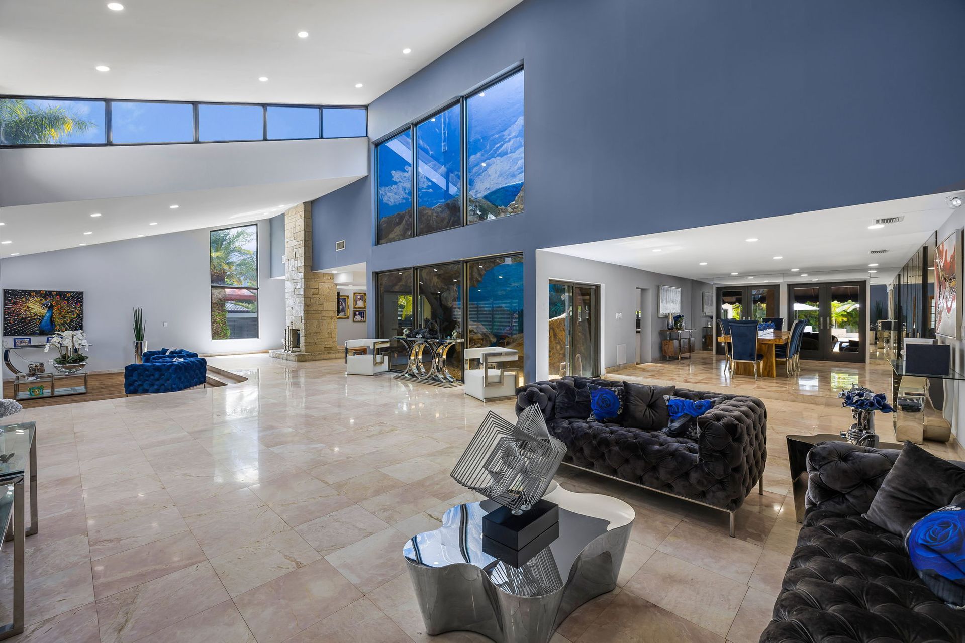 Spacious living room with blue walls, large windows, modern furniture, and reflective marble floors.