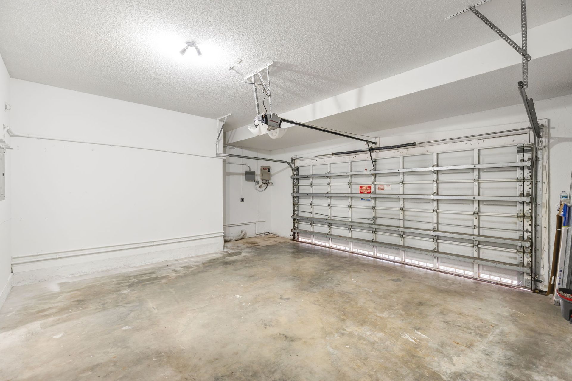 A clean, empty garage with white walls, a concrete floor, and an overhead garage door opener.