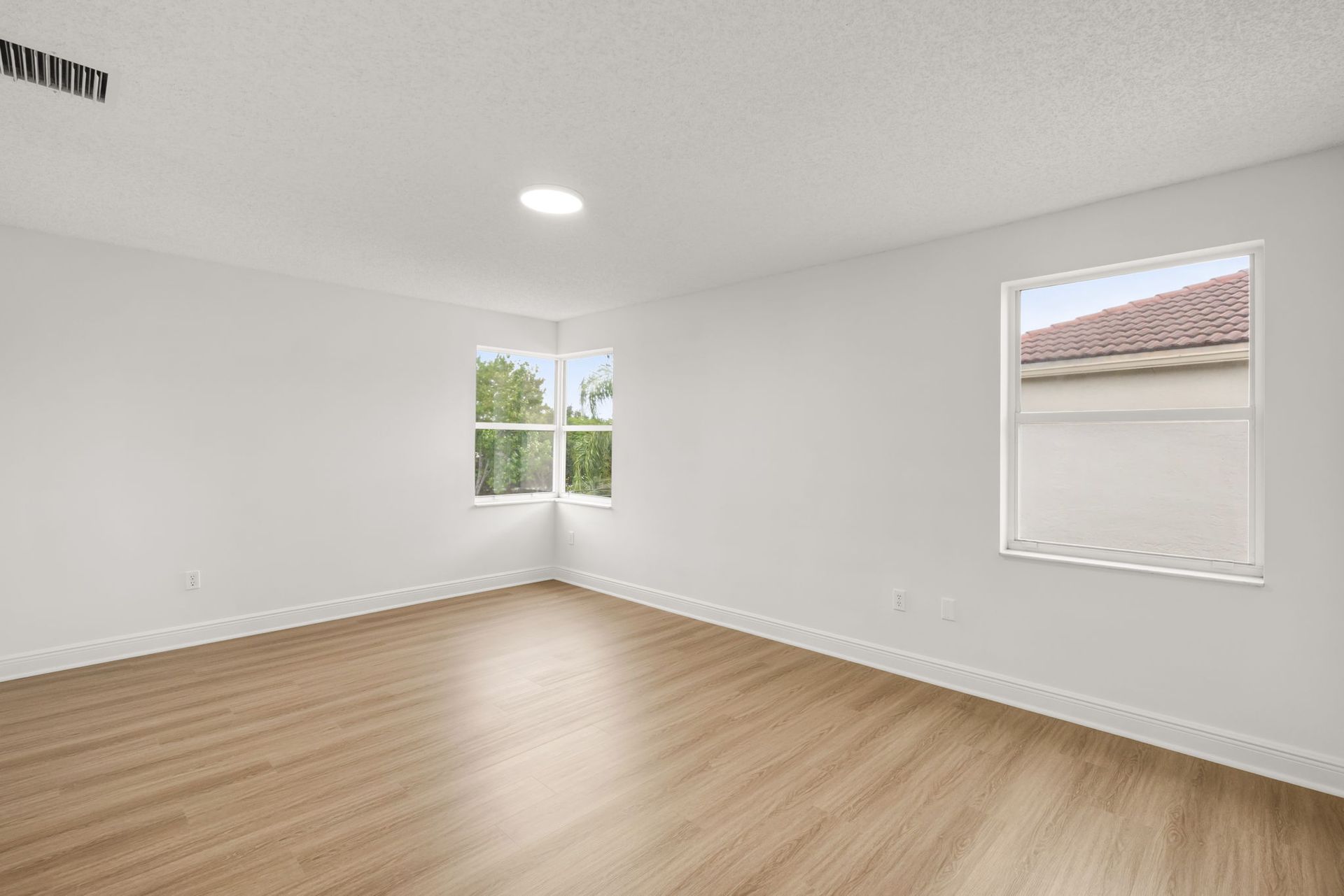 Empty room with white walls, light wood-look floors, a corner window, and a single square window on the right wall.