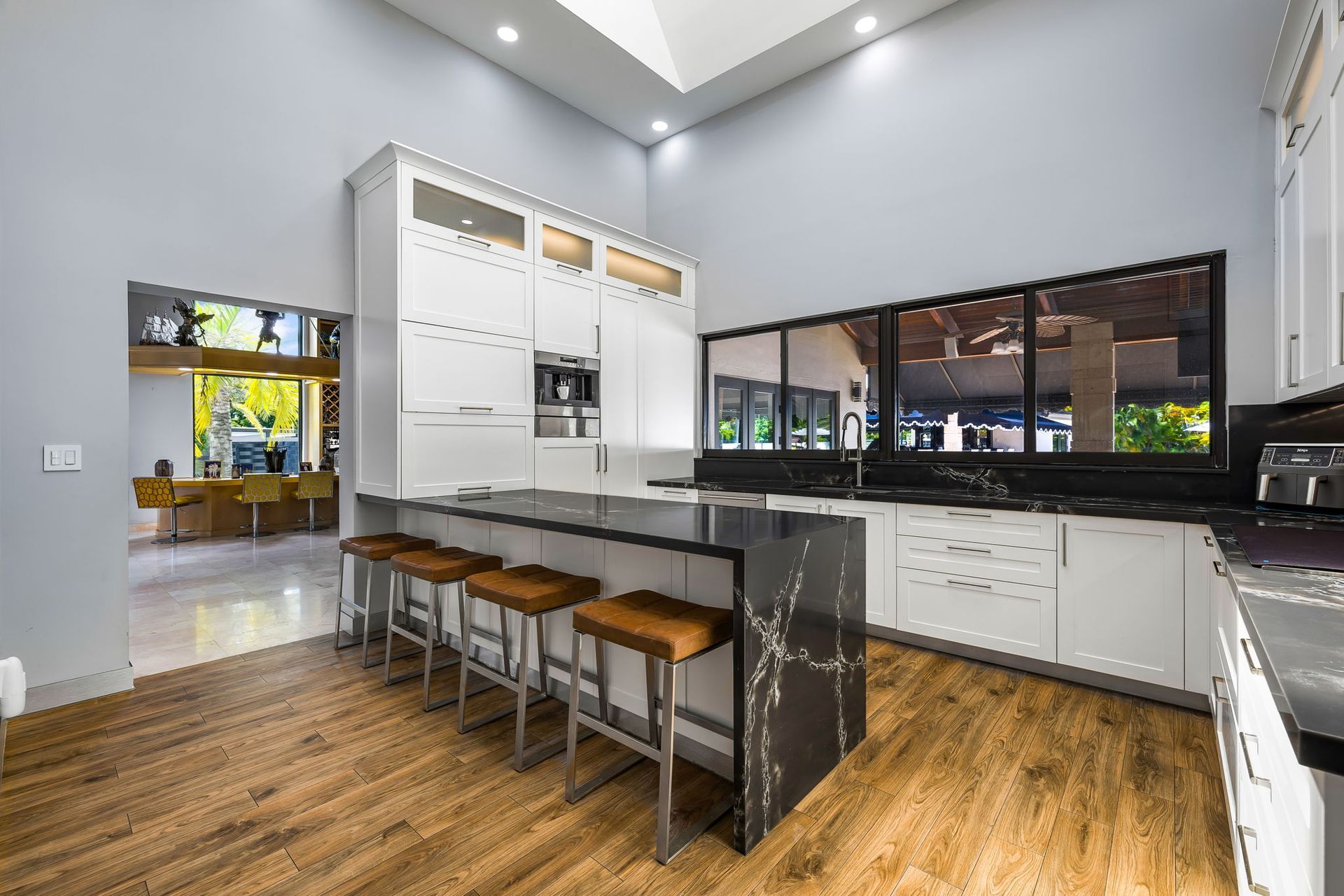 Modern kitchen with white cabinets, island with barstools, and a large window overlooking a patio.