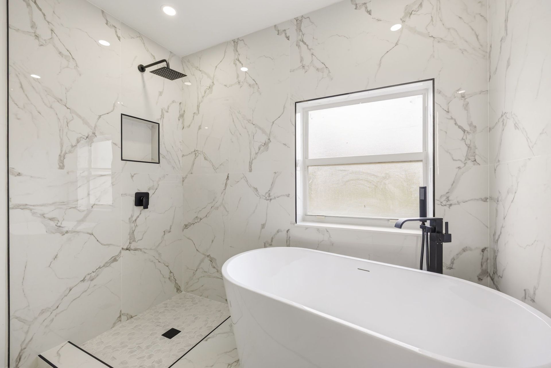 Modern bathroom with a white marble walk-in shower, black fixtures, and a freestanding soaking tub by a window.