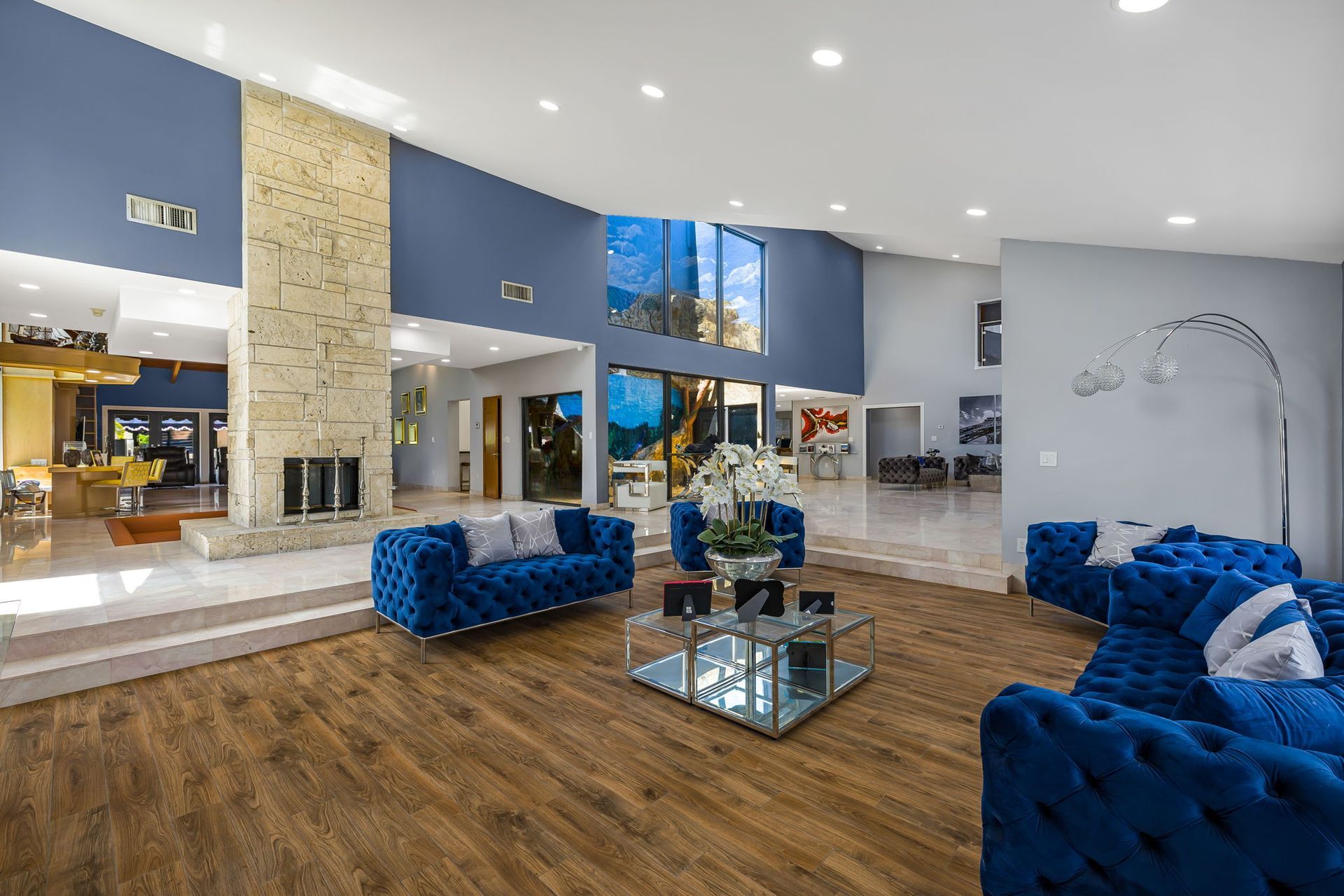 Spacious living room with blue sofas, hardwood floors, and a large stone fireplace.
