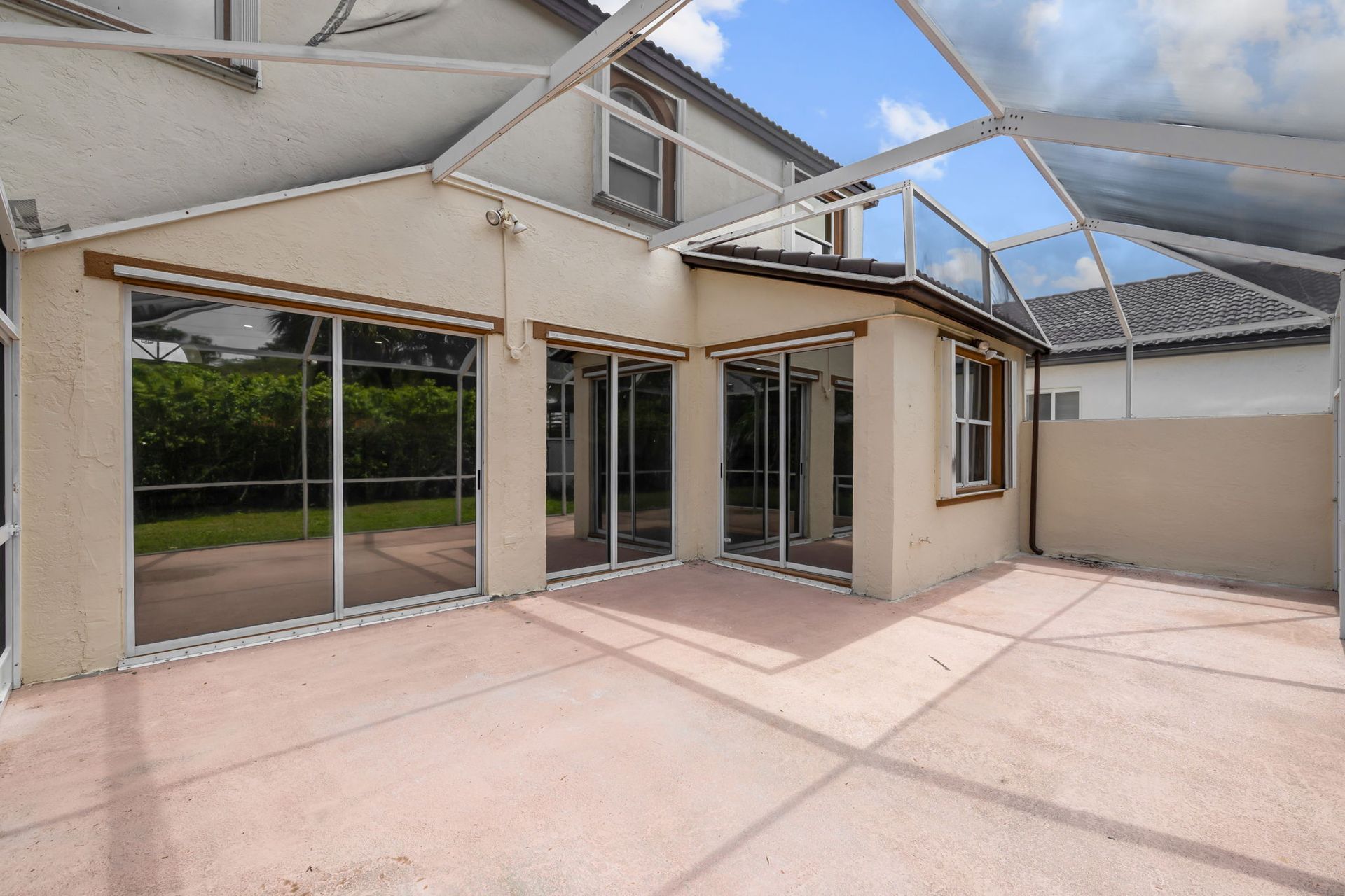 A beige house exterior with large glass sliding doors and a screened-in patio area under a white metal enclosure.