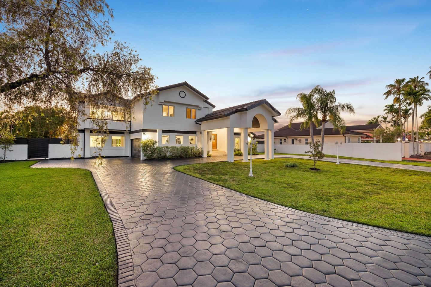 Modern two-story house with a paved driveway, green lawn, and a covered entry at sunset