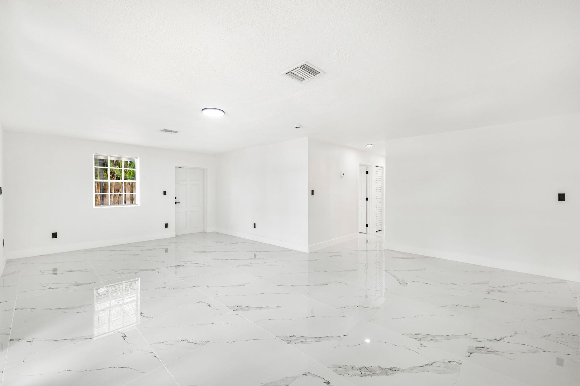 Empty room with white walls, marble floors, window, and two doors.