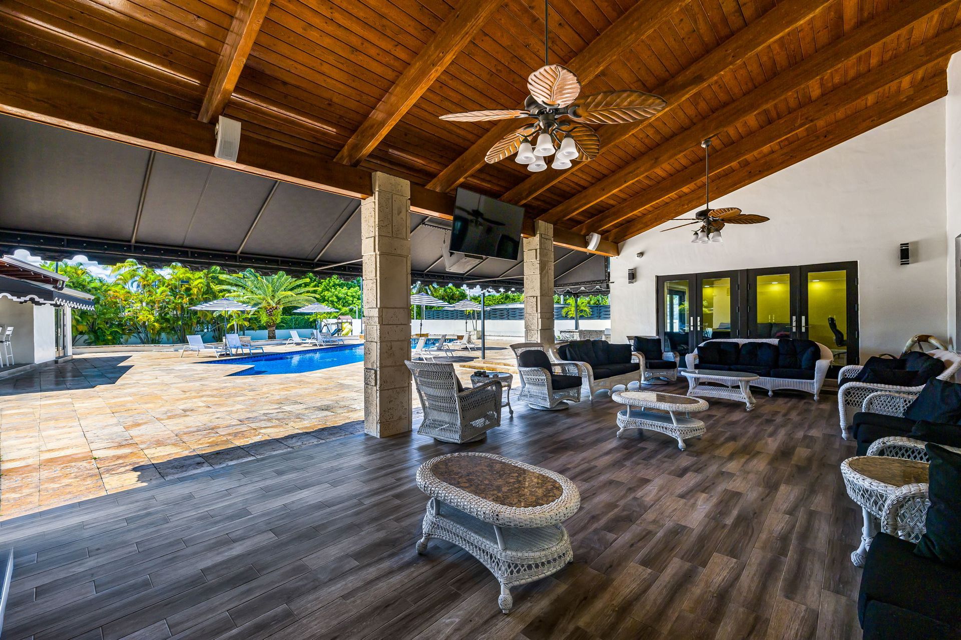 Covered patio with seating, wood floor, pool view.