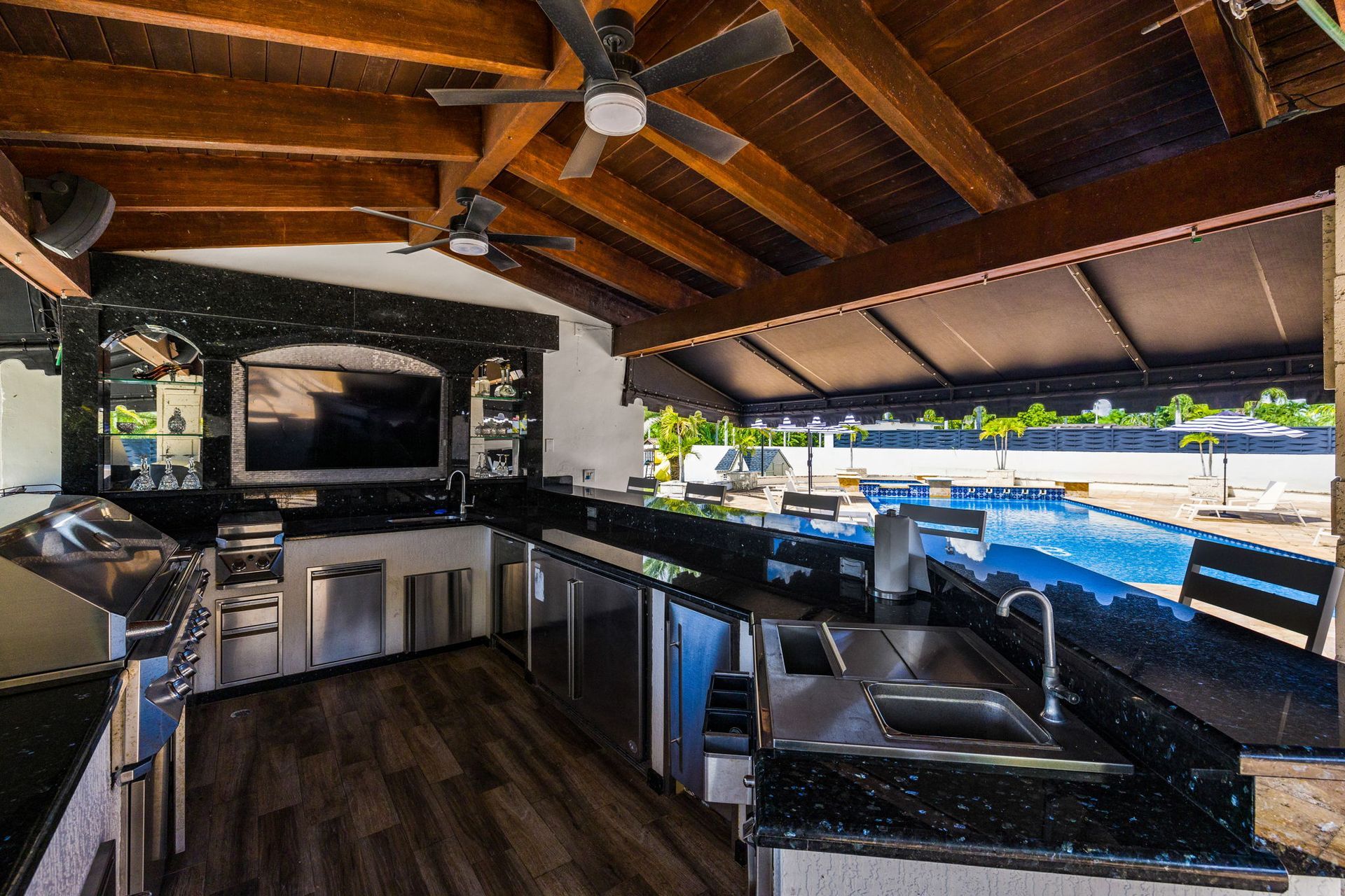 Outdoor kitchen with black granite countertops, a TV, and a view of a pool.