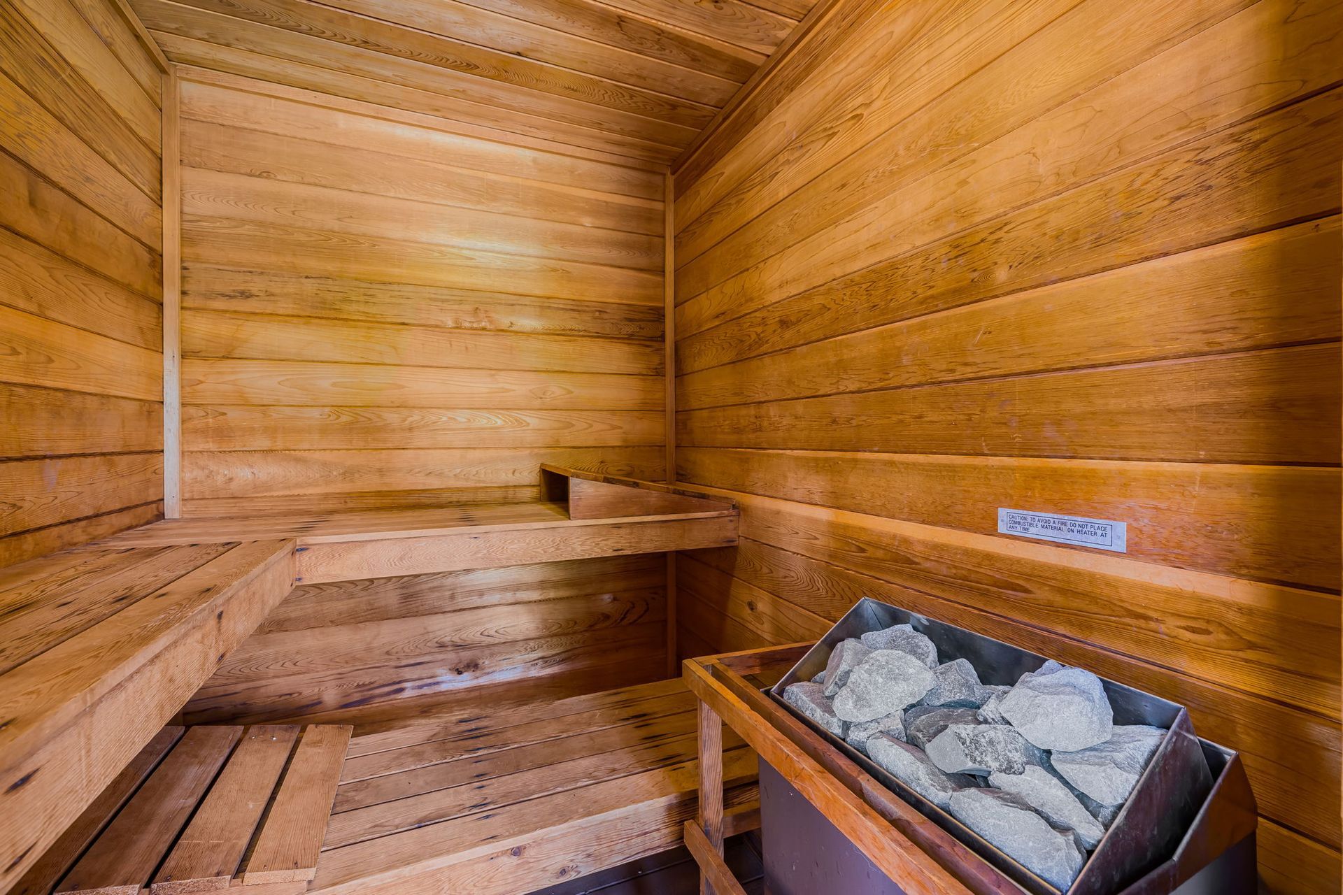 Wooden sauna interior with benches and a heater filled with rocks.
