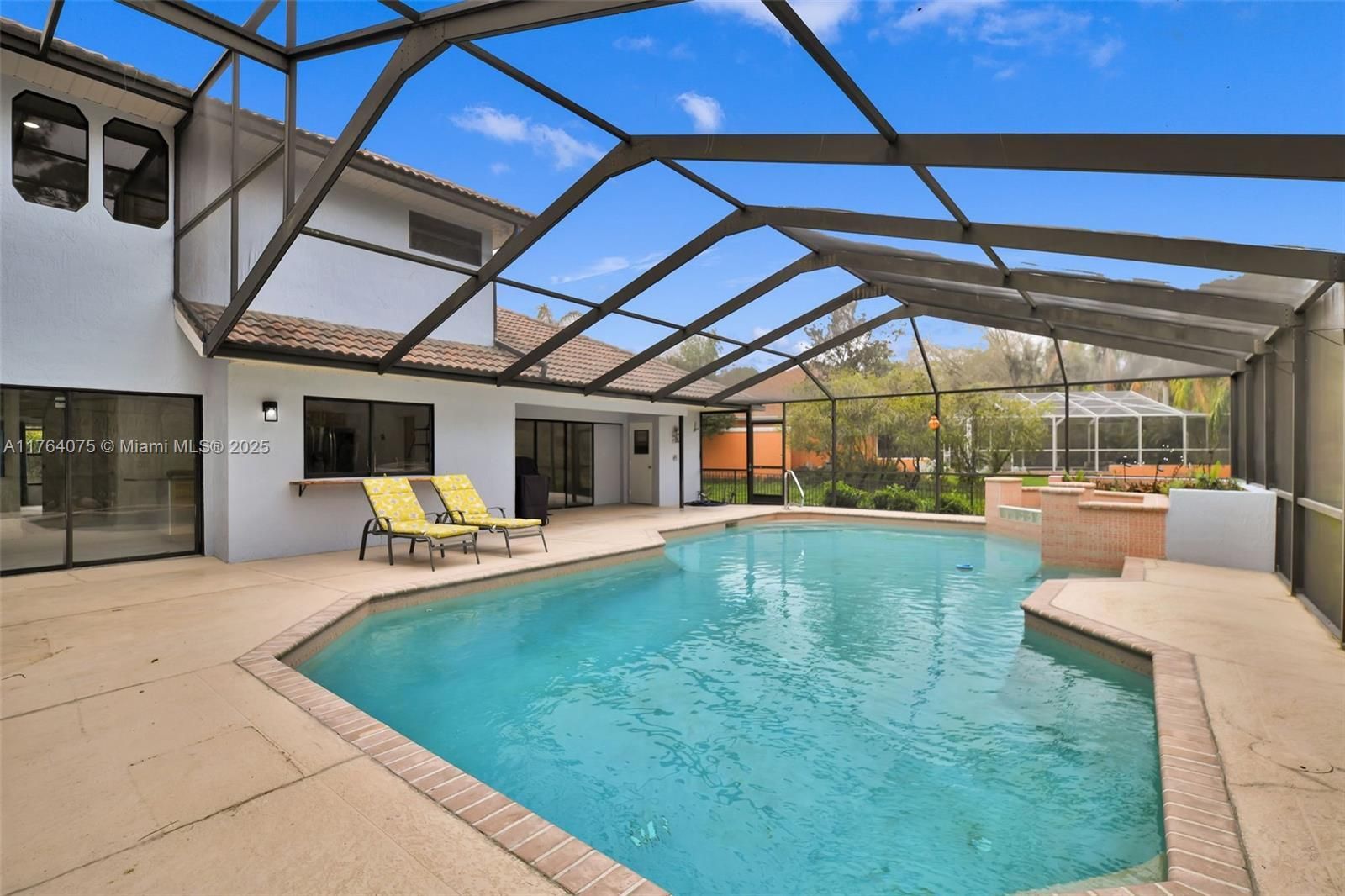 Swimming pool in a screened patio, with a house in the background. Two lounge chairs are by the pool.