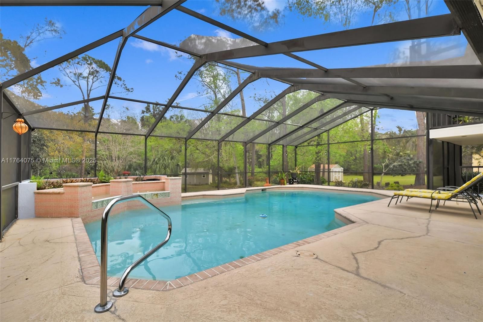 Swimming pool enclosed by a screen in a backyard with lounge chairs and greenery.