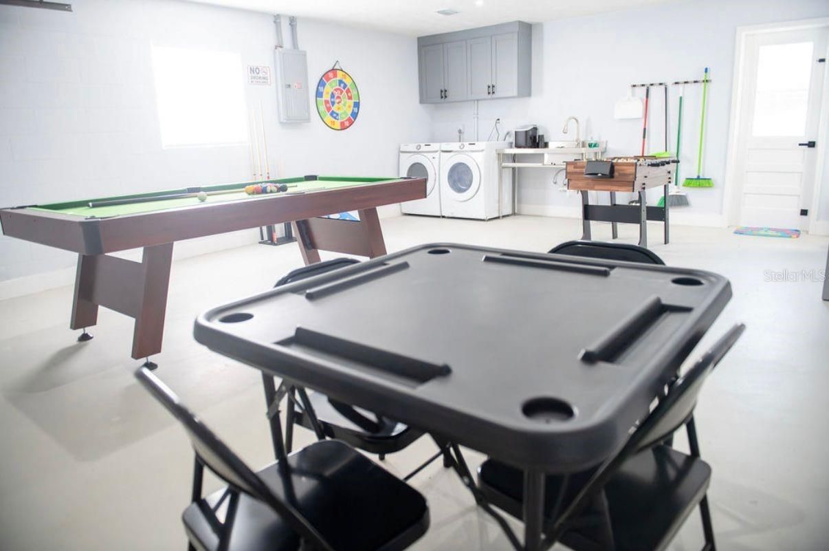 Sala de juegos luminosa con mesa de billar, mesa de ping-pong, futbolín y zona de lavandería.