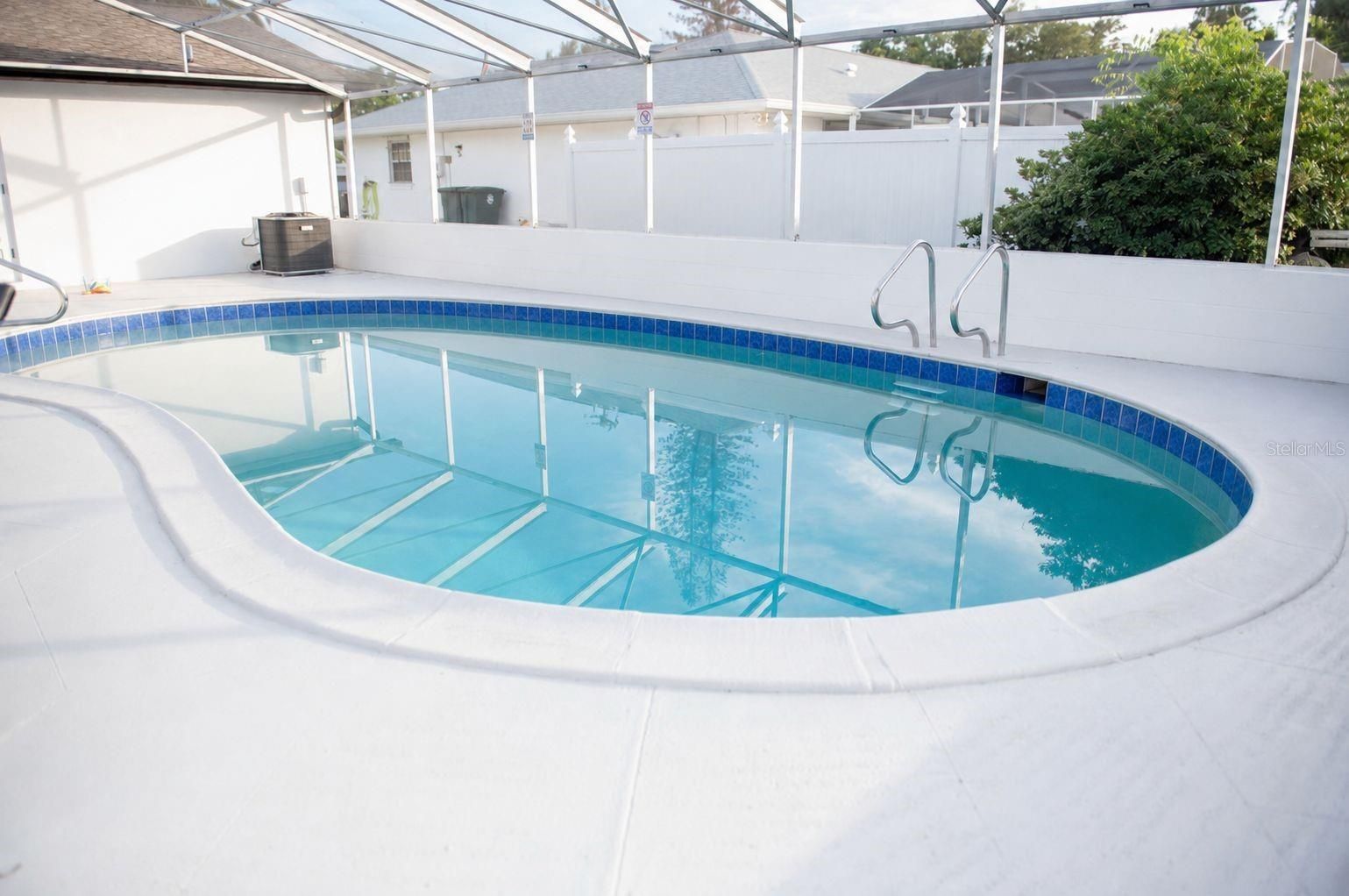 Piscina cubierta con agua azul y terraza de baldosas blancas bajo un patio cubierto.