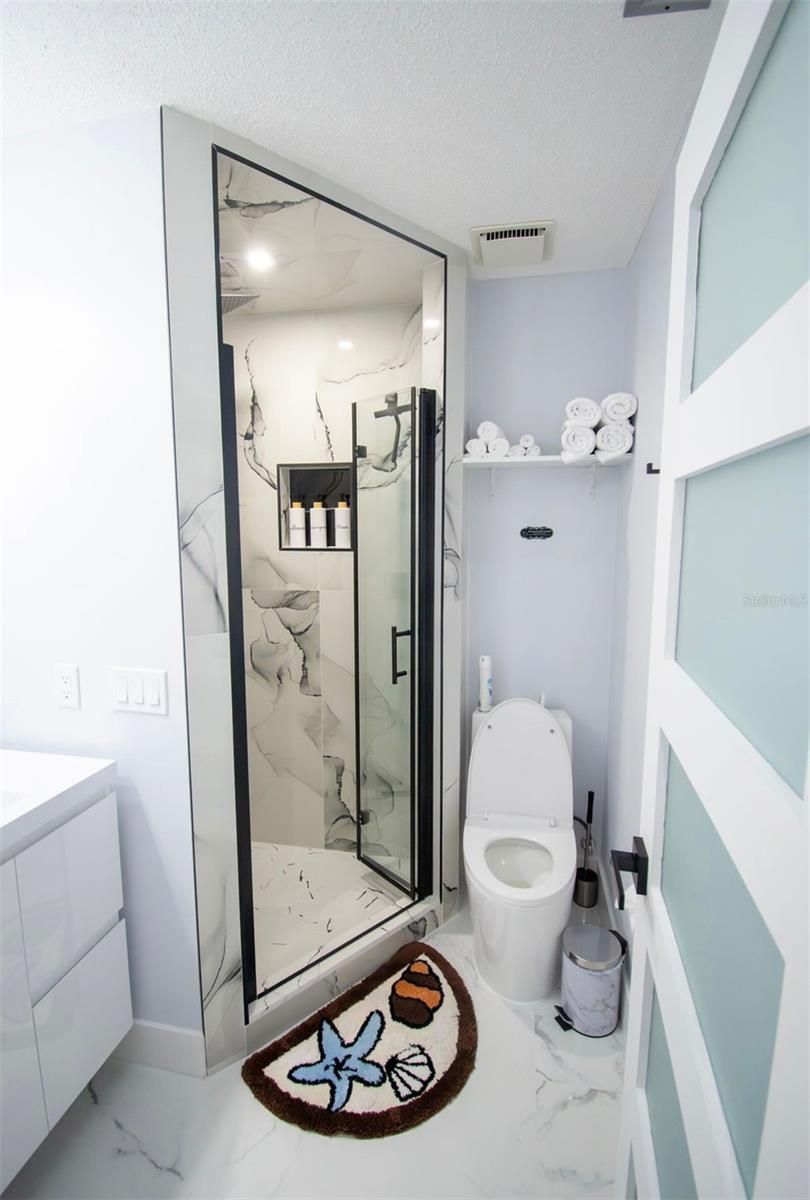 Baño compacto con ducha de cristal, inodoro y puerta a rayas blancas y azules.
