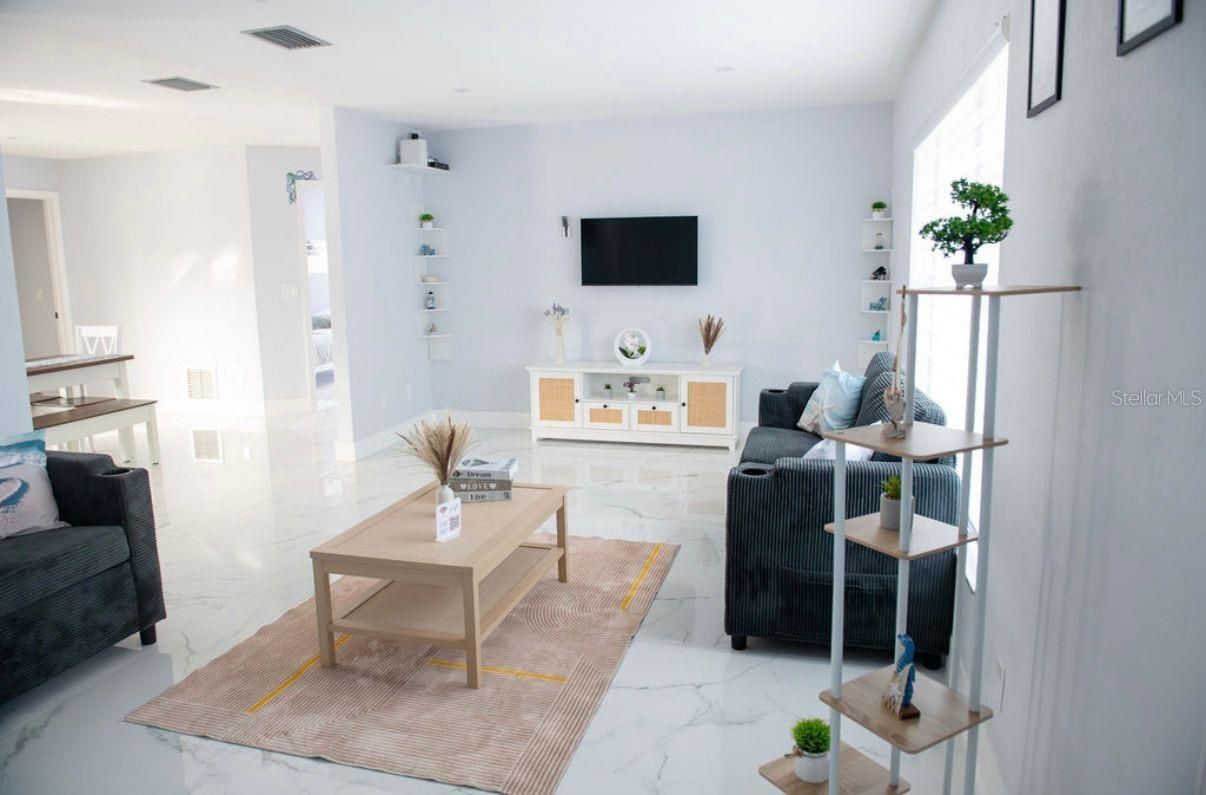 Luminoso salón moderno con paredes blancas, sofás grises, mesa de centro, televisor y alfombra beige.