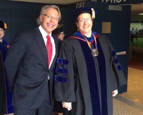 A man in a suit and tie stands next to a woman in a graduation gown