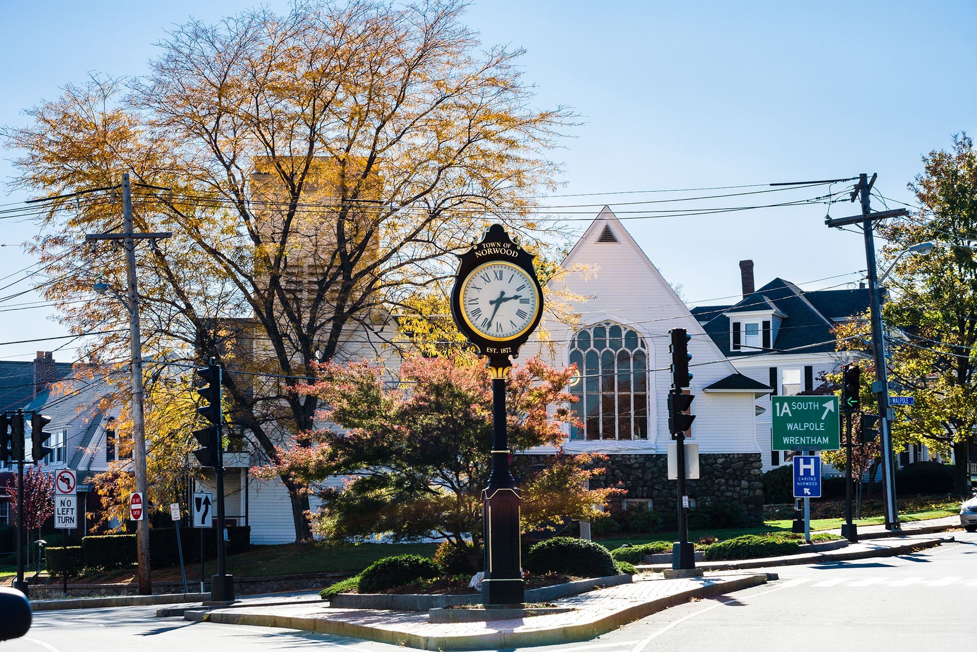 Town square clock near autumn trees and white buildings on a sunny day