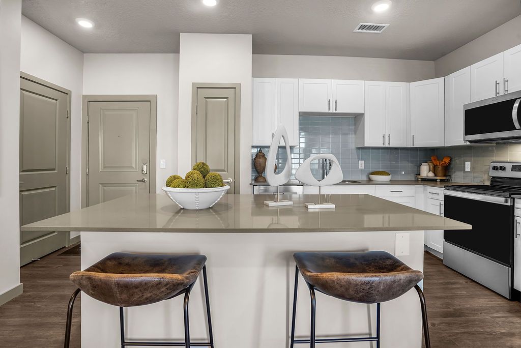 Modern kitchen in an apartment with a large island, white cabinets, and stainless steel appliances.