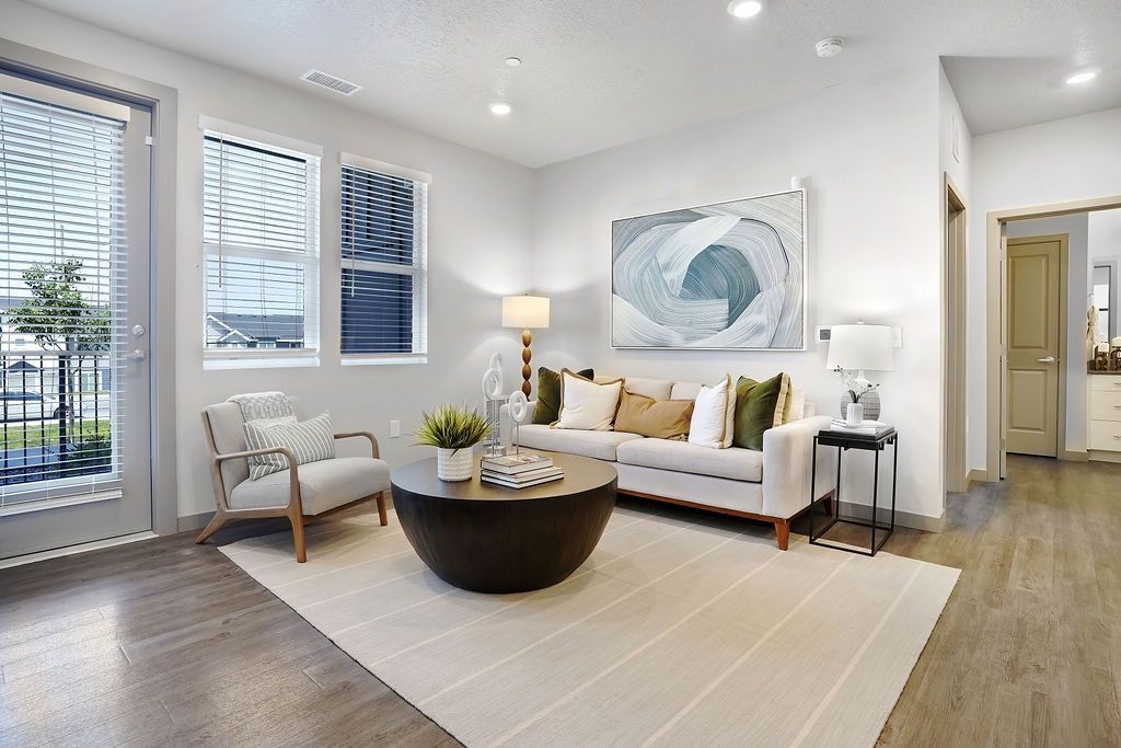 Bright living room with a beige sofa, armchair, round coffee table, and large windows.