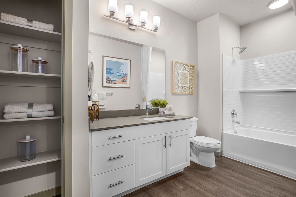 Bright apartment bathroom with white vanity, gray counter, mirror, toilet, and tub/shower.