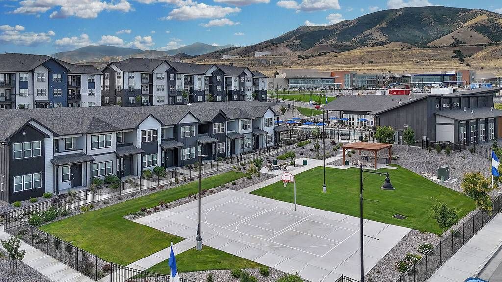 Aerial view of a multifamily community with townhomes, a basketball court, and a green lawn.