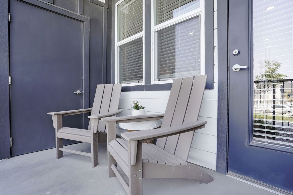 Two gray Adirondack chairs on a small porch outside a blue door and window.
