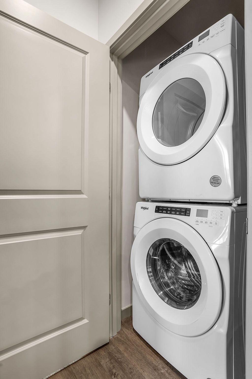 Stacked washer and dryer in a narrow laundry closet beside a door.