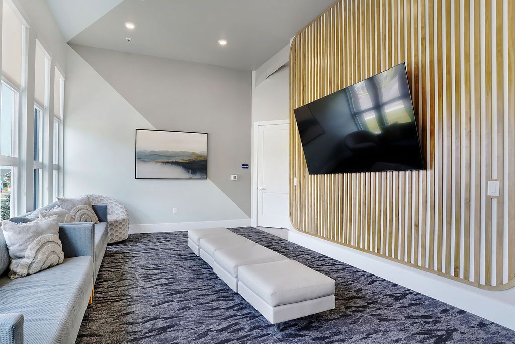 Modern communal lounge with large windows, a sectional sofa, and a wall-mounted TV on a vertical wood panel.