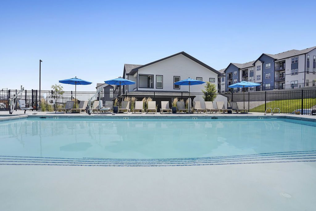 Outdoor pool area at a residential community with lounge chairs and blue umbrellas.