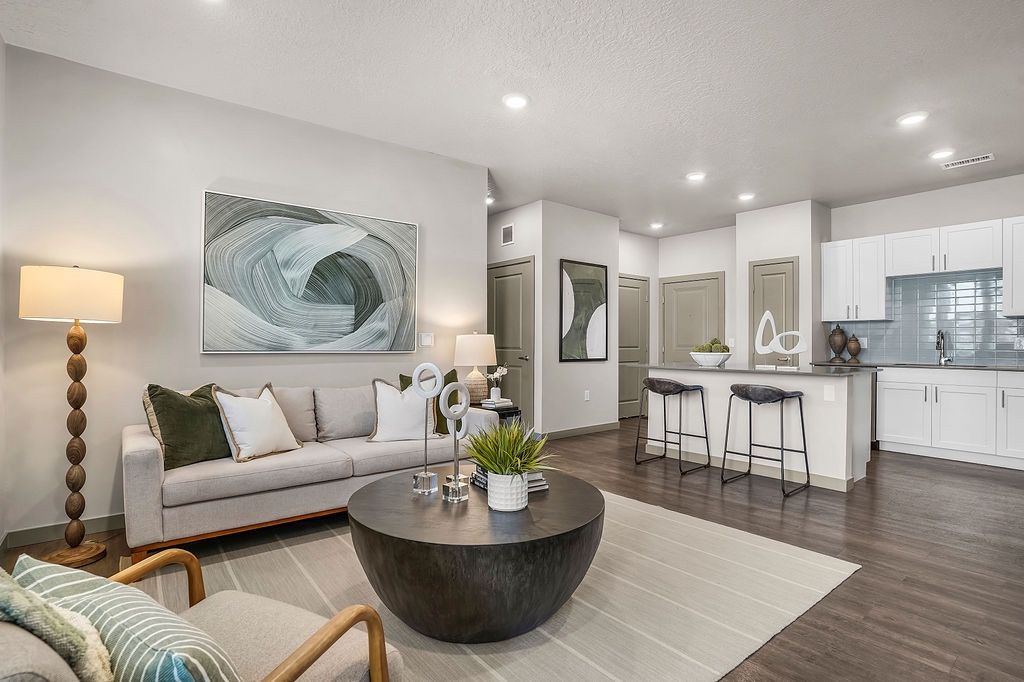 Open-concept living room and kitchen in a modern apartment, featuring a gray sofa, round coffee table, and bar stools.