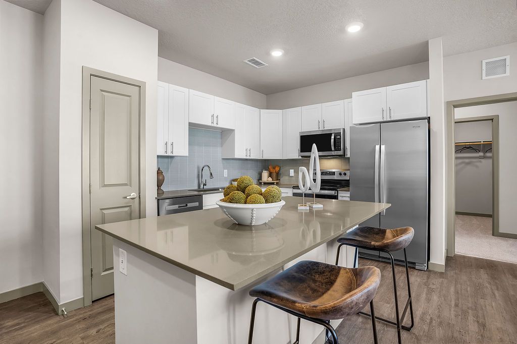 Open-concept kitchen in a modern apartment with white cabinets, stainless appliances, and an island.
